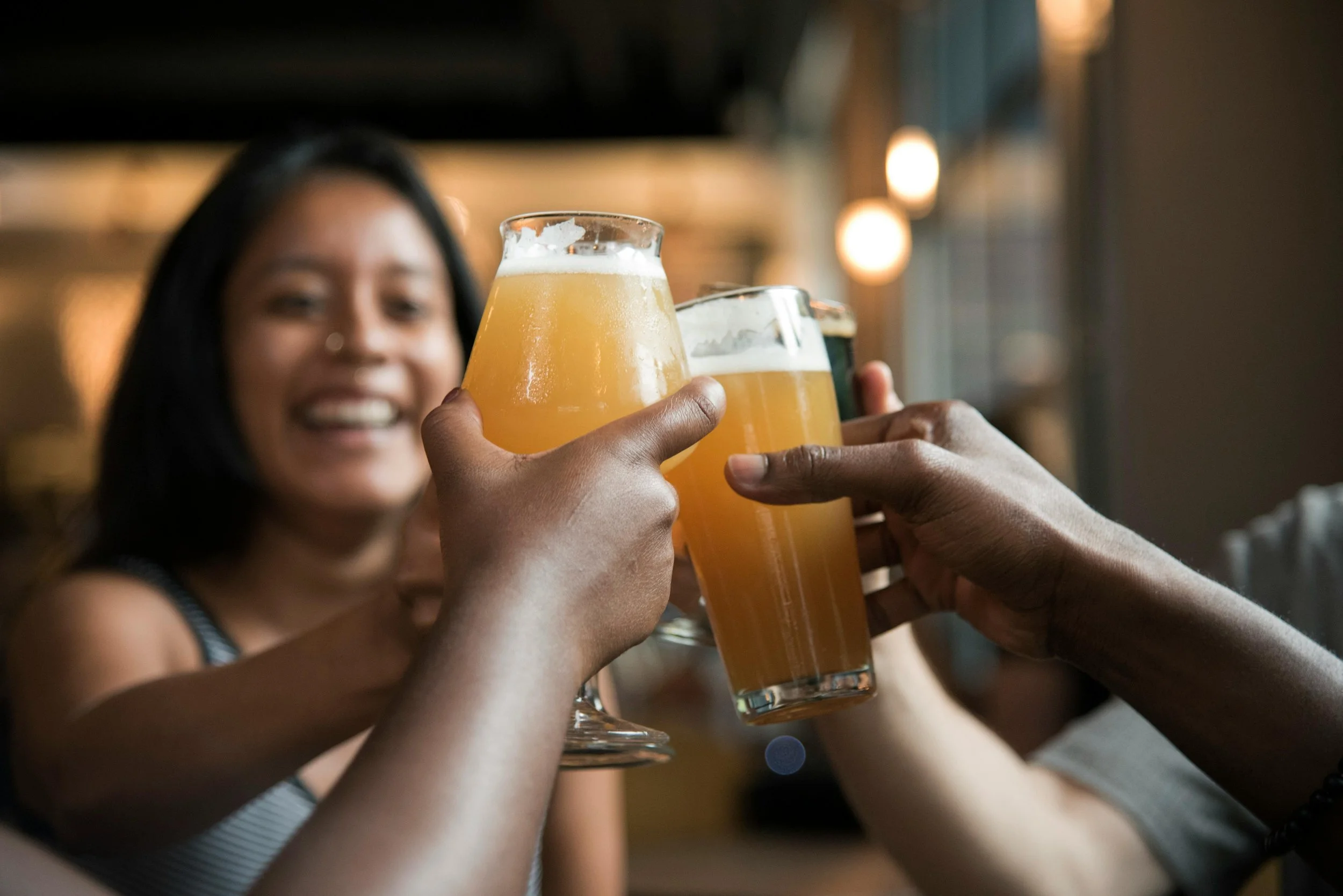 People clinking glasses of beer in a toast in a bar with a smiling woman in the background.