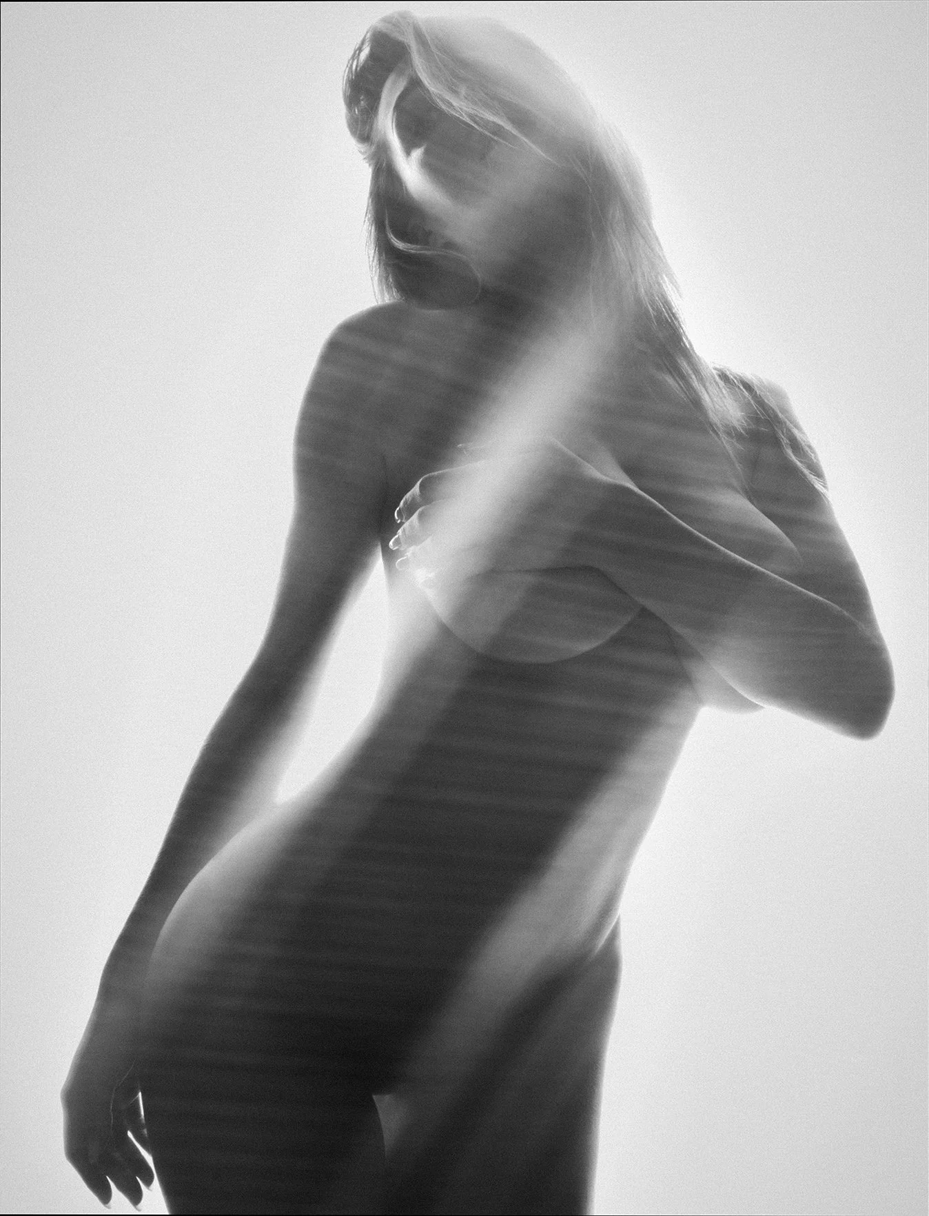Black and white photo of a woman with wind-blown hair, holding her left arm across her chest and smiling with eyes closed.