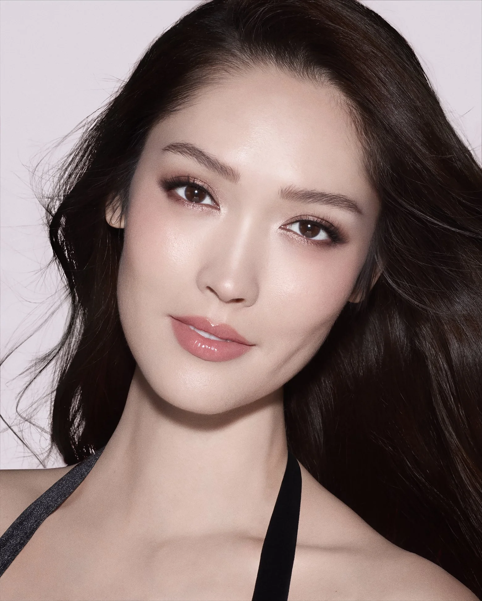 Close-up portrait of a woman with long dark hair, wearing makeup with neutral tones, and a black strap top.