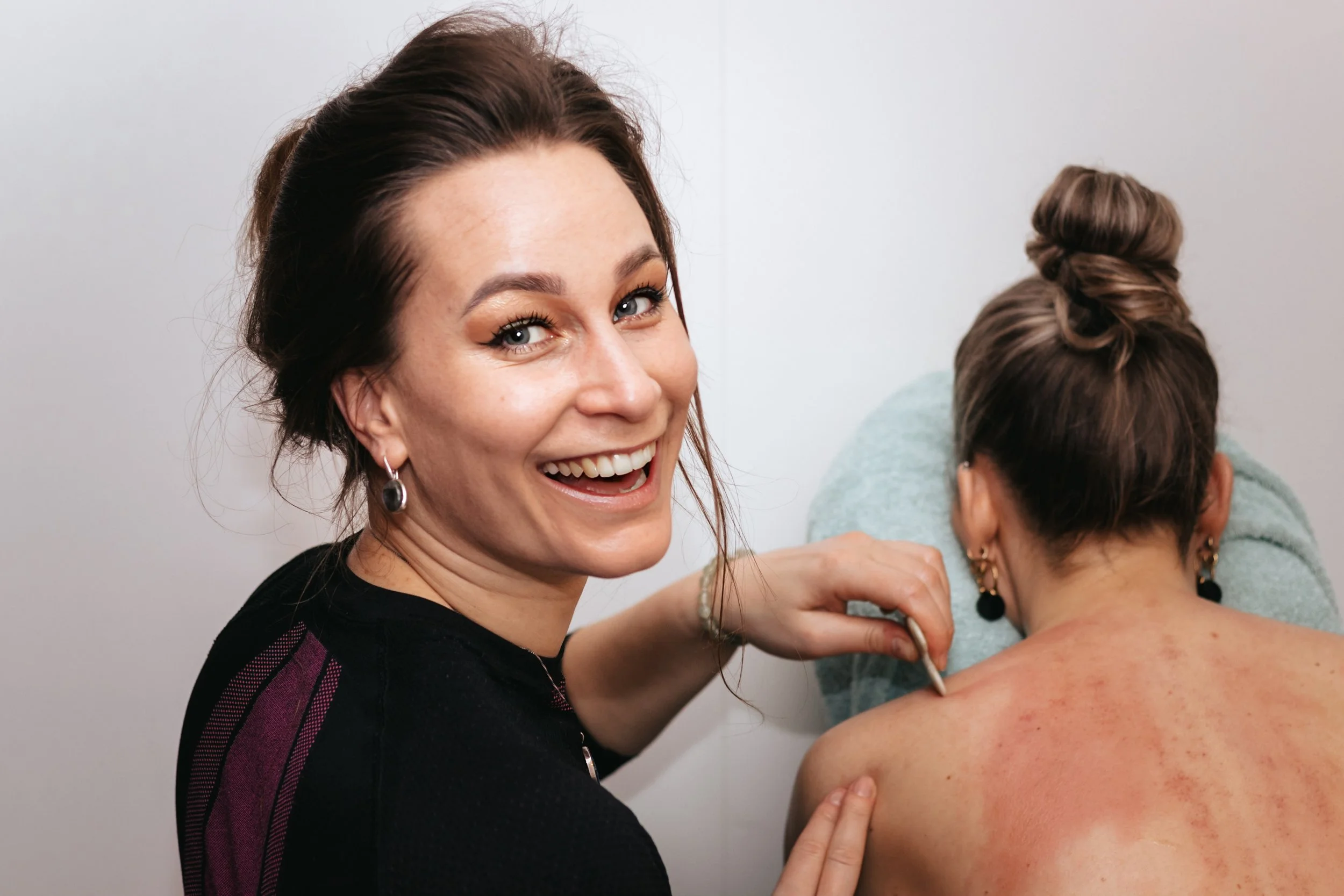 Portrait of a woman who is smiling during a gua-sha body massage session of her client, another woman, face-dawn in a massage chair.
