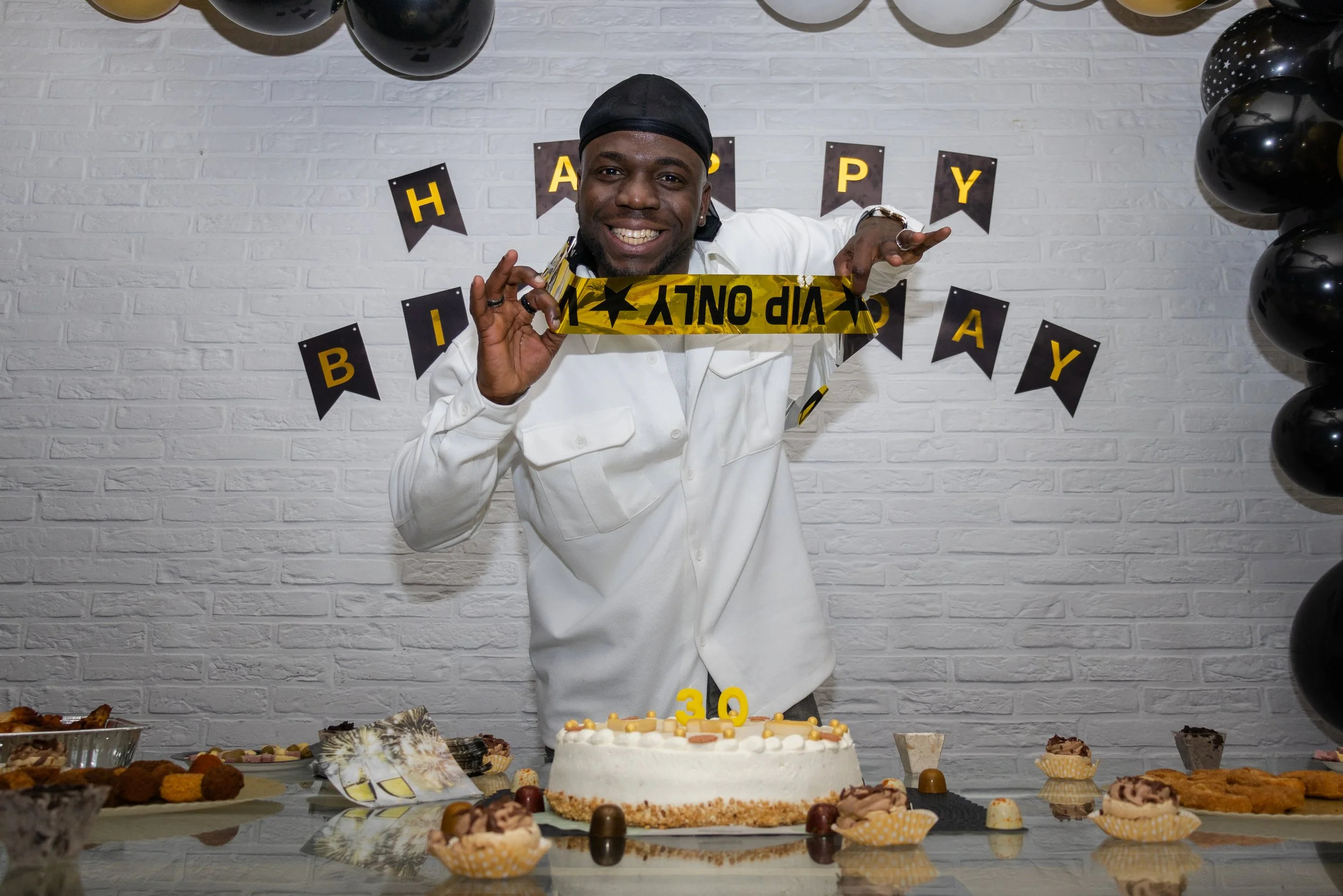 Event picture of a man standing behind his birthday cake and smiling, holding his "VIP ONLY" sash in a party mood.