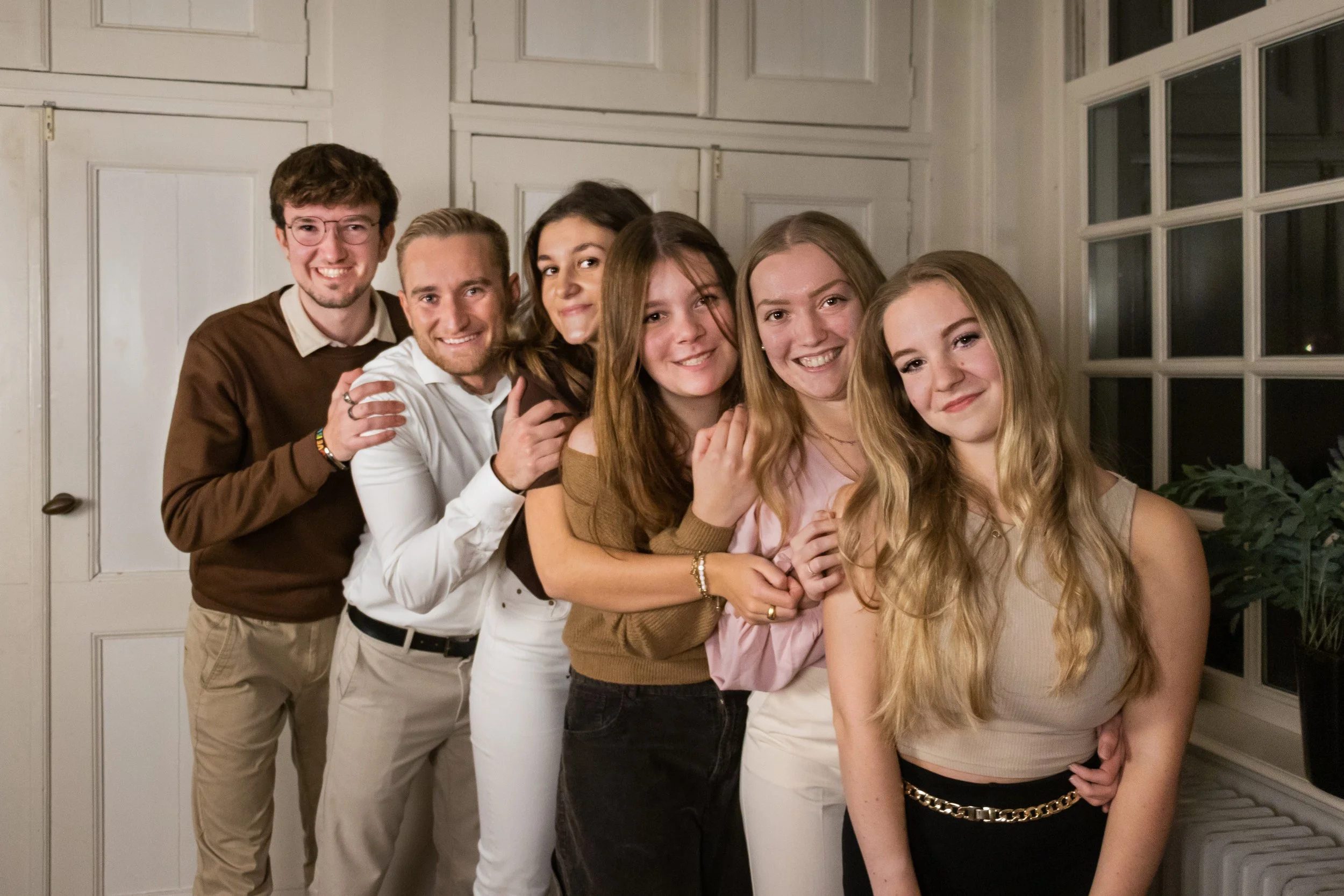 Family picture with six young people, 2 brothers, 2 sisters and 2 female cousins, all standing in a row order, smallest girl in the front and tallest guy in the back, looking in the camera.