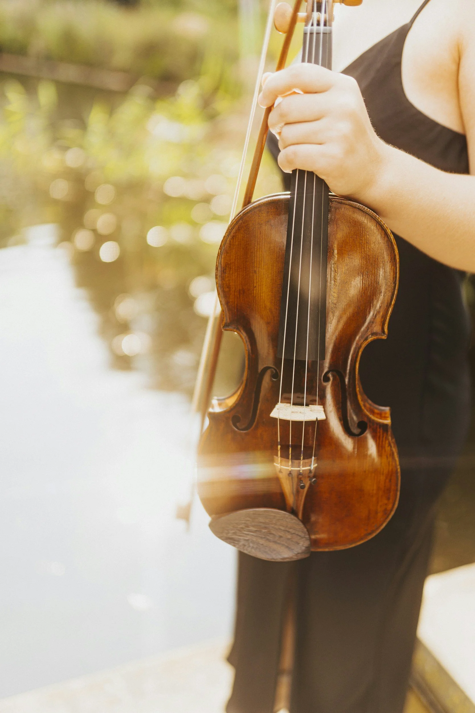 Person holding a violin and bow near a body of water outdoors.