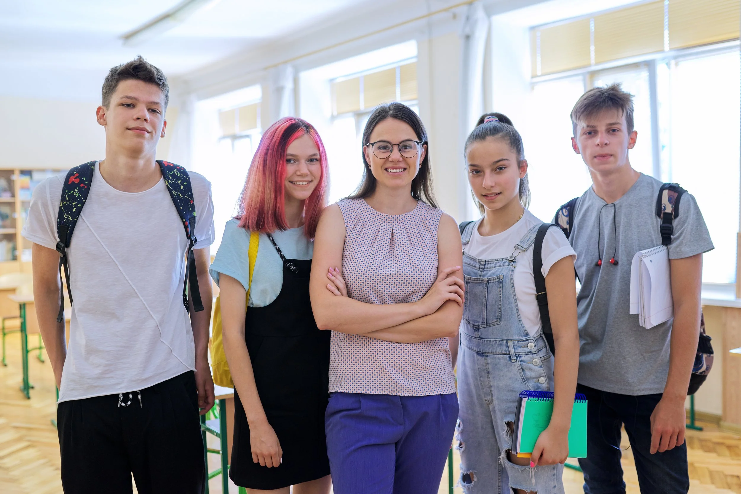 A group of five students and a teacher standing together in a classroom, smiling at the camera.