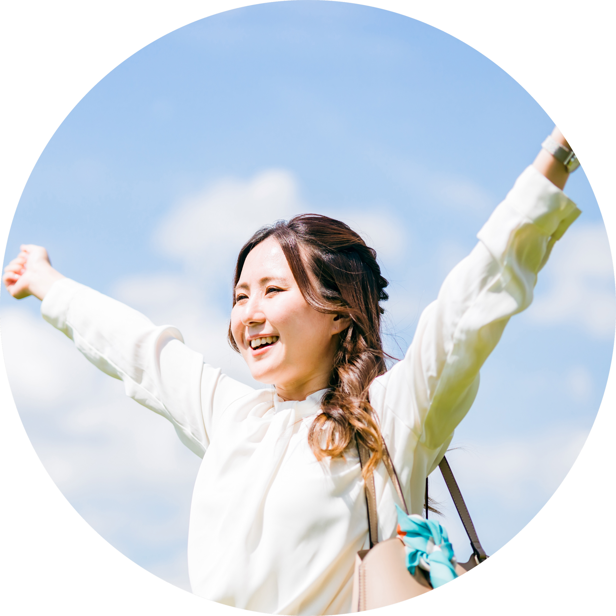 A smiling woman with arms raised outdoors against a blue sky with clouds, wearing a white jacket and carrying a beige purse with a blue bow.