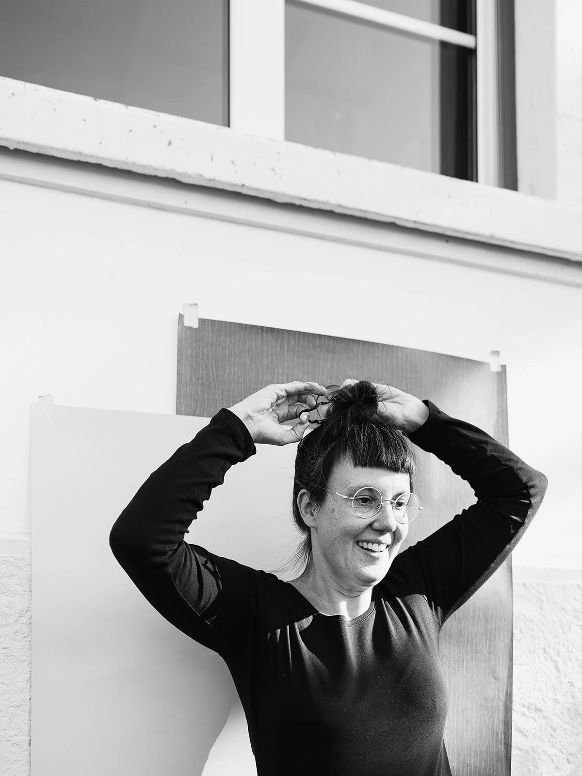 Eine lachende Frau mit Brille steckt ihre Haare hoch. 