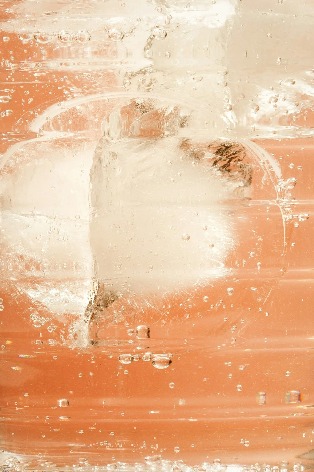 Close-up of a glass filled with bubbly, fizzy, pink-colored beverage with ice cubes inside.