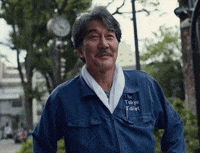 Smiling man in a blue jacket outdoors with trees and streetlights in the background