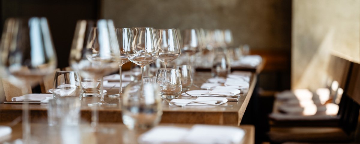 Leere eleganten Esszimmer der Weingrün Rotisserie mit gedecktem Tisch, Weingläser, Wasser- und Weingläser, weißen Servietten, Tellersets und schwarzen Stühlen.