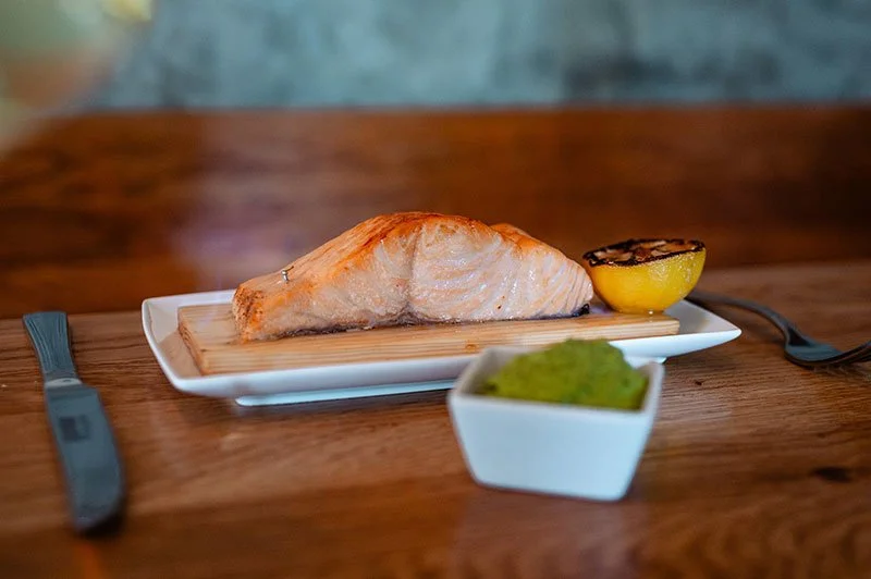 Gegrillter finnischer Flammlachs mit Zitronenscheibe und grüner Soße auf einem Teller