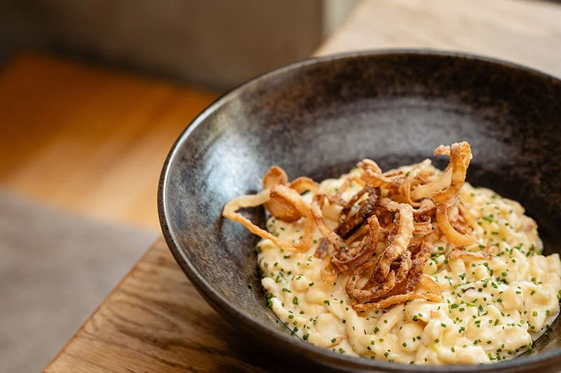 Käsespätzle mit Zwiebelringen in einer schwarzen Schale