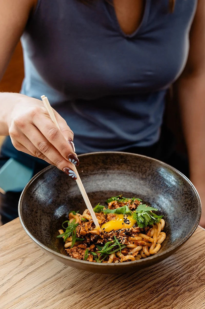 Person, die eine Schüssel mit Hühner Bolognese, Ei, Frühlingszwiebeln, Koriander und Sesamsamen isst.