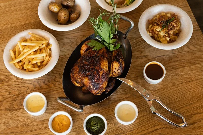 Gegrilltes Paderborner Landhuhn mit Beilagen wie Pommes, Kartoffeln, Gemüse und verschiedenen Soßen auf einem Holztisch