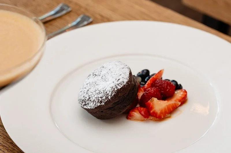 Warmer Schokoladenkuchen mit Puderzucker, frische Erdbeeren, Heidelbeeren und Erdbeersoße auf einem weißen Teller