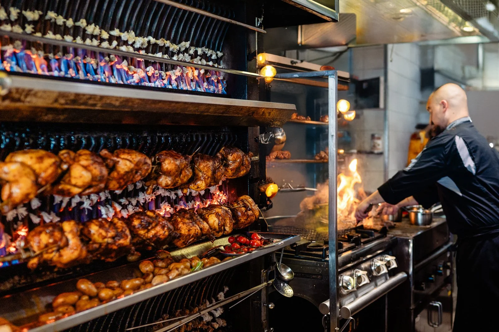 Koch am Flammenwand Grill beim Grillen von Hähnchen über offener Flamme in der Rotisserie Weingrün.