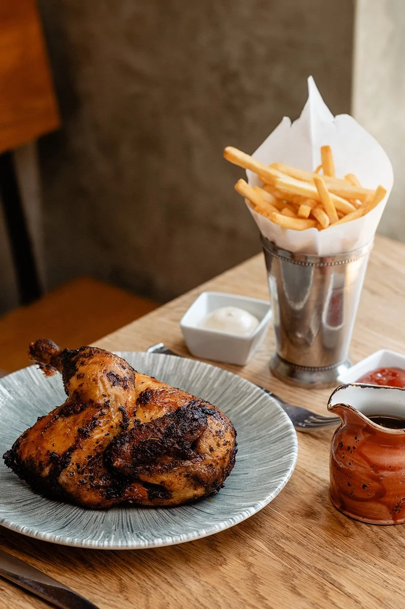 Gegrilltes Hähnchen mit Pommes Frites, eine Soße in einer kleinen Schale, und Ketchup auf einem Tisch.