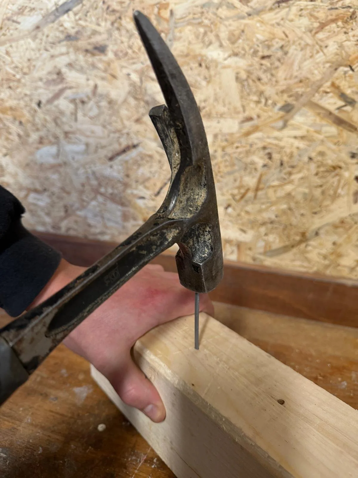 Une personne utilise un marteau pour frapper un clou à travers un morceau de bois.