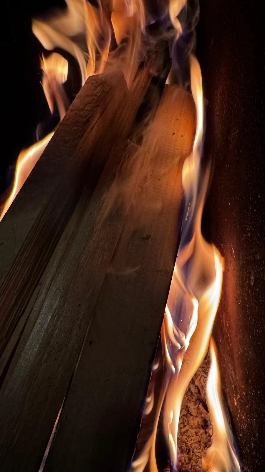 Deux morceaux de bois en train de brûler avec des flammes jaunes et orange accentuées par la chaleur intense.