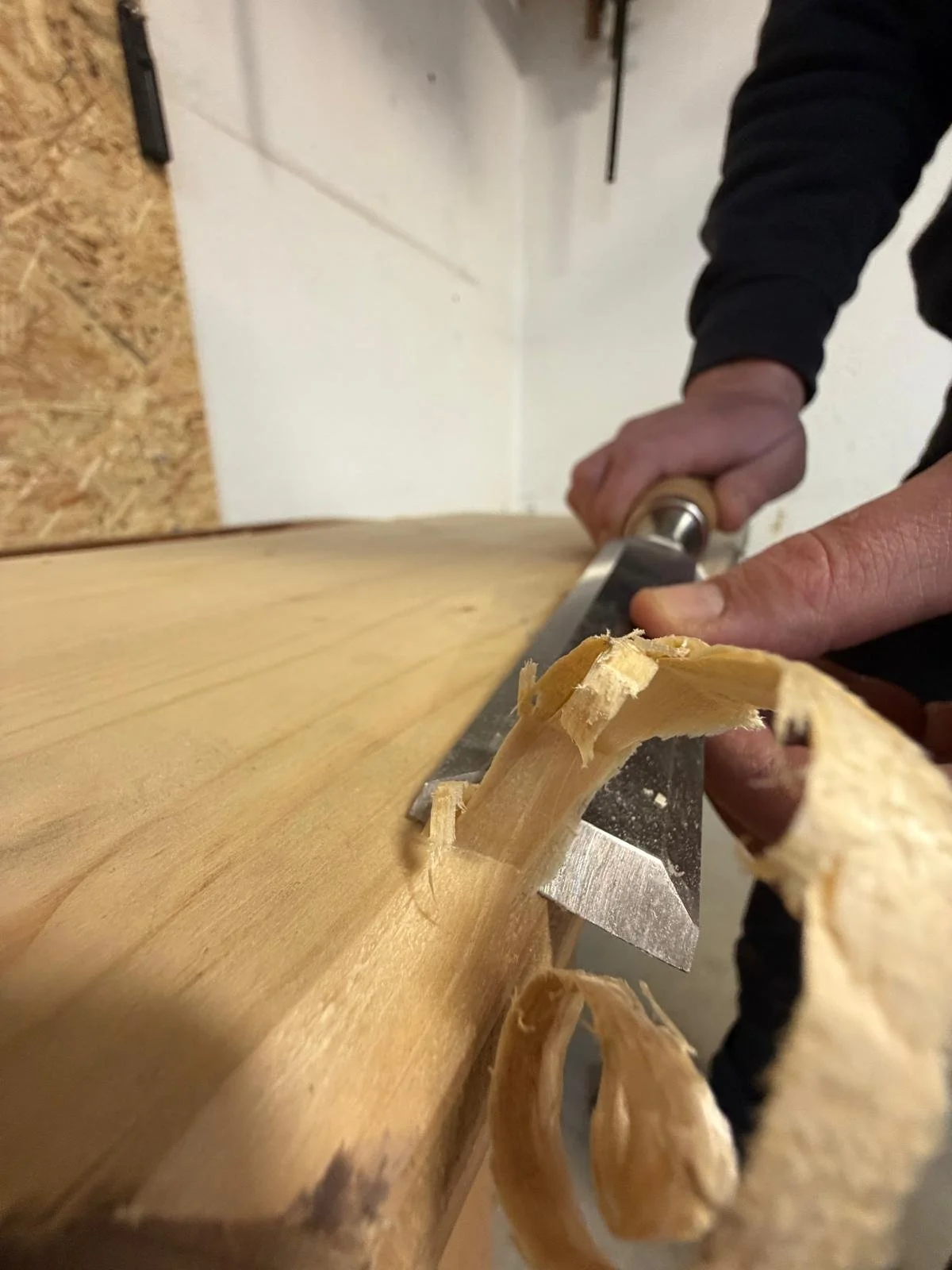 Une personne en train de scier du bois avec une scie. Le bois est posé sur une surface de travail, et la personne tient la scie avec une main, tandis que l'autre main guide le bois.