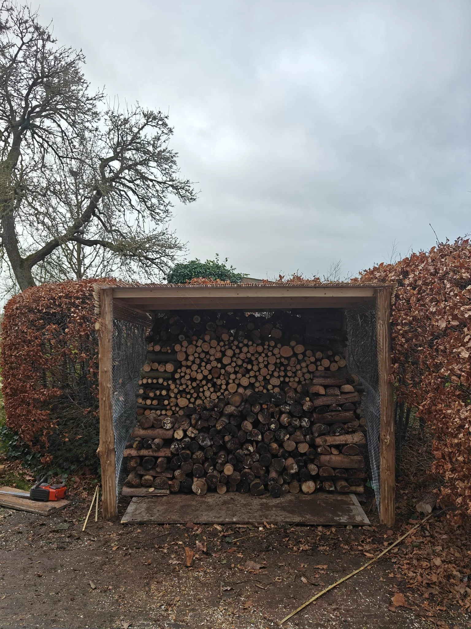 Een houten houtopslag met gesorteerd hout onder een dak.