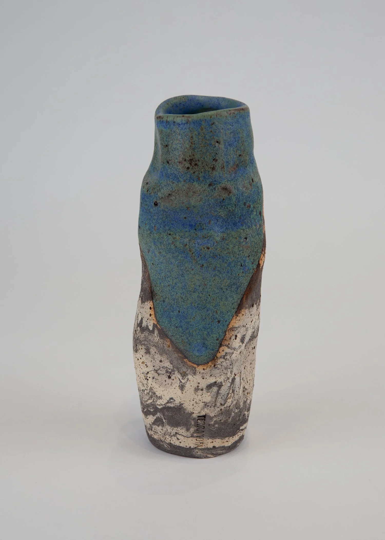 Ceramic vase with a textured surface, featuring a blue-green glazed upper section and a lower section with black, white, and gray swirling patterns.