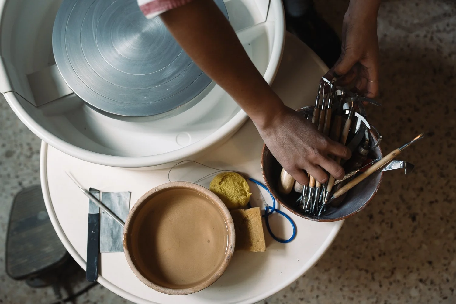 Person handling jewelry tools over a white table with a small clay bowl, soaked sponge, and cleaning supplies, near a large ultrasonic jewelry cleaner.