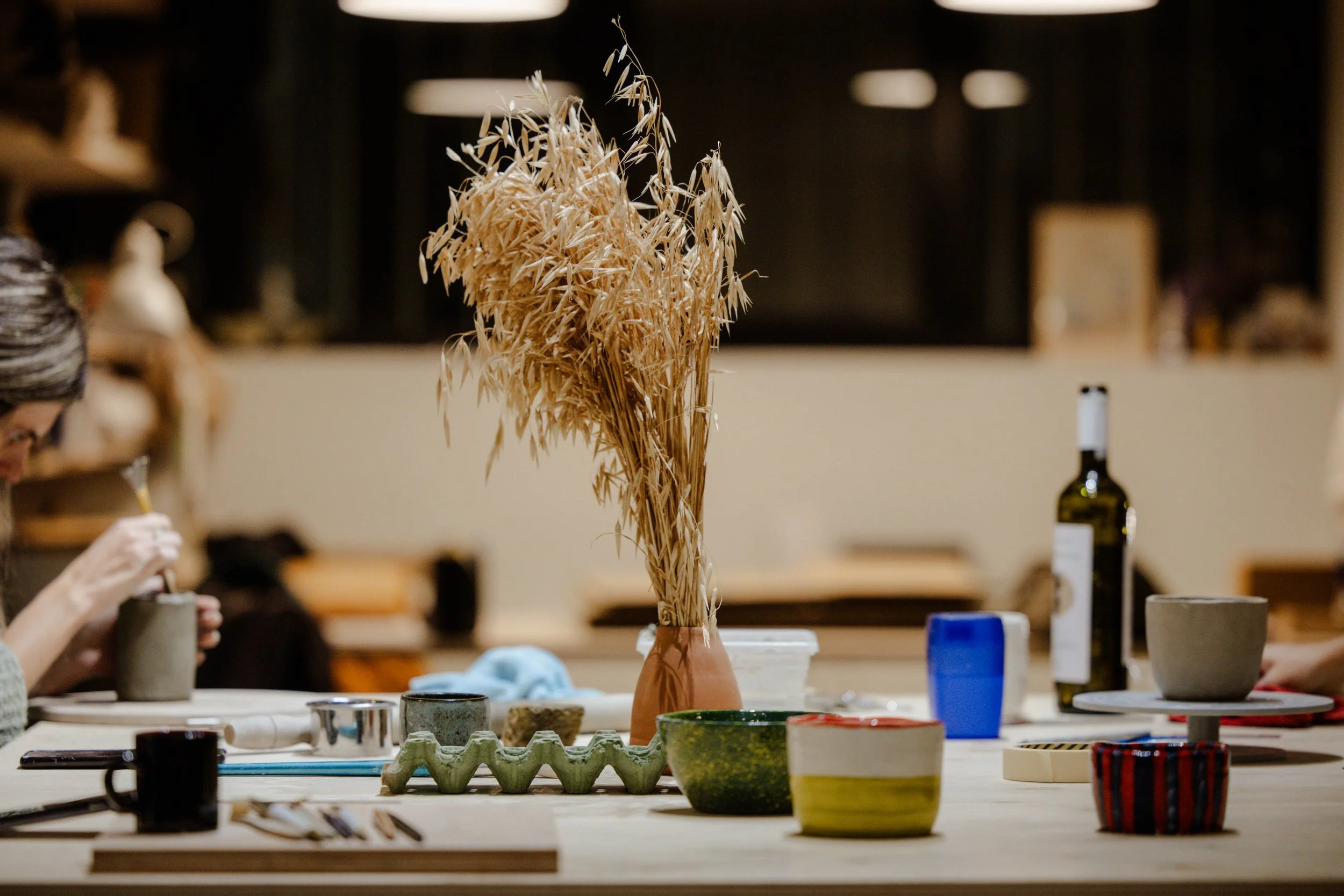 A display of pottery and ceramics on a table with a large dried plant arrangement in a terracotta vase in the center.