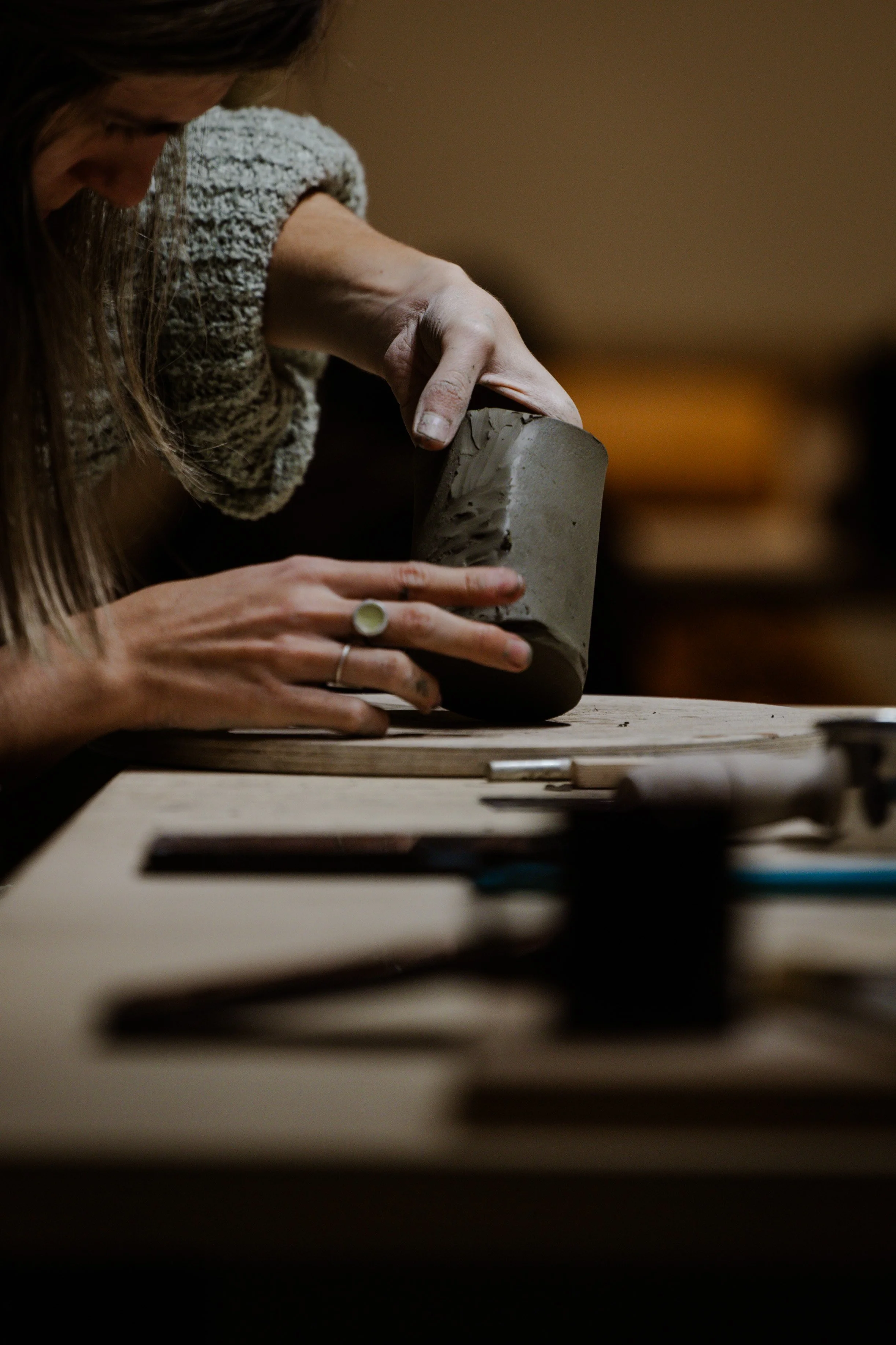 Person shaping a clay sculpture on a wooden table, focused on their work.
