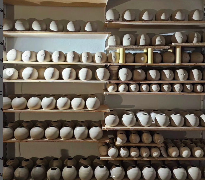 Shelves filled with unfinished ceramic pots in a workshop.