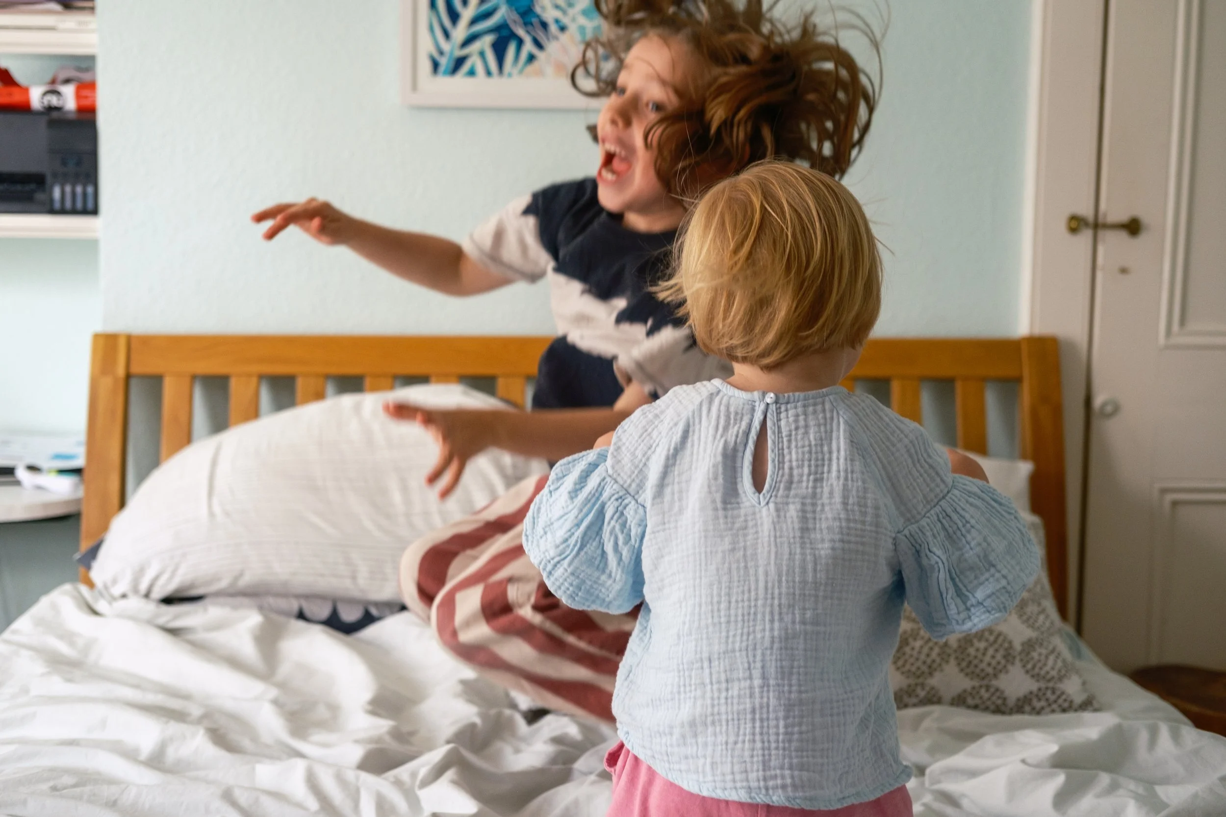 Two children playing and jumping on a bed with an adult in a bedroom.