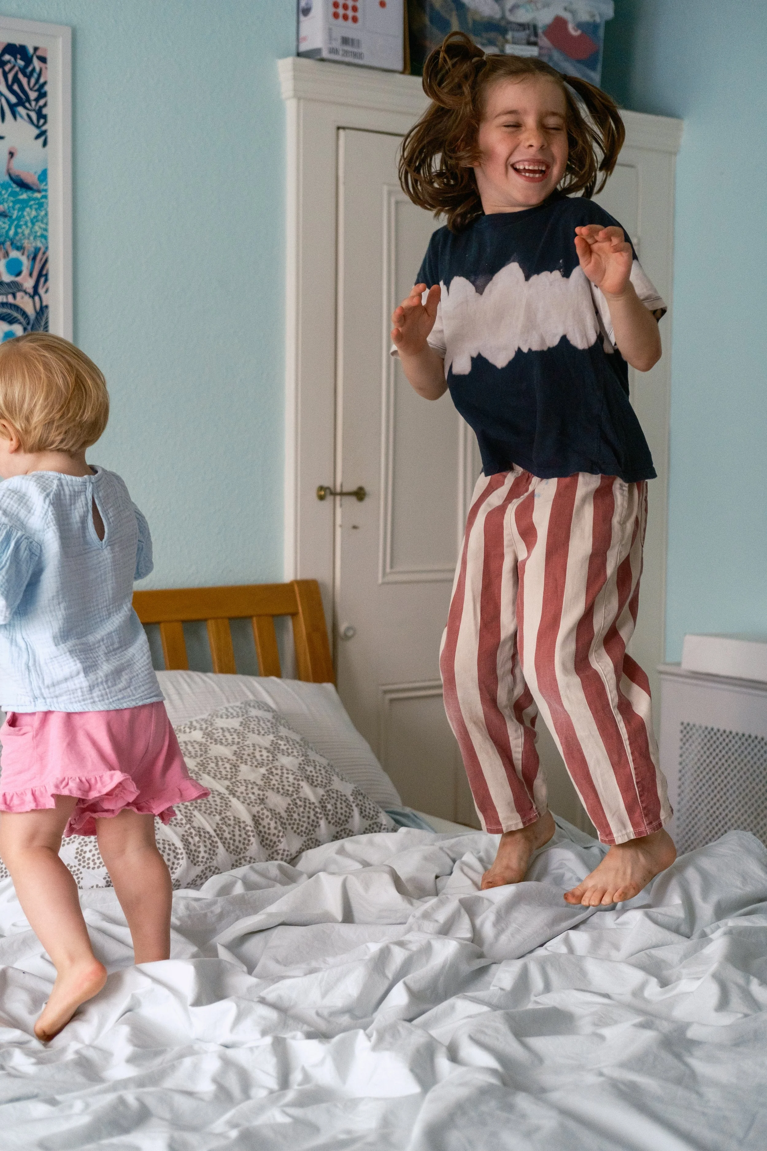 Two young children playing and jumping on a bed in a bedroom