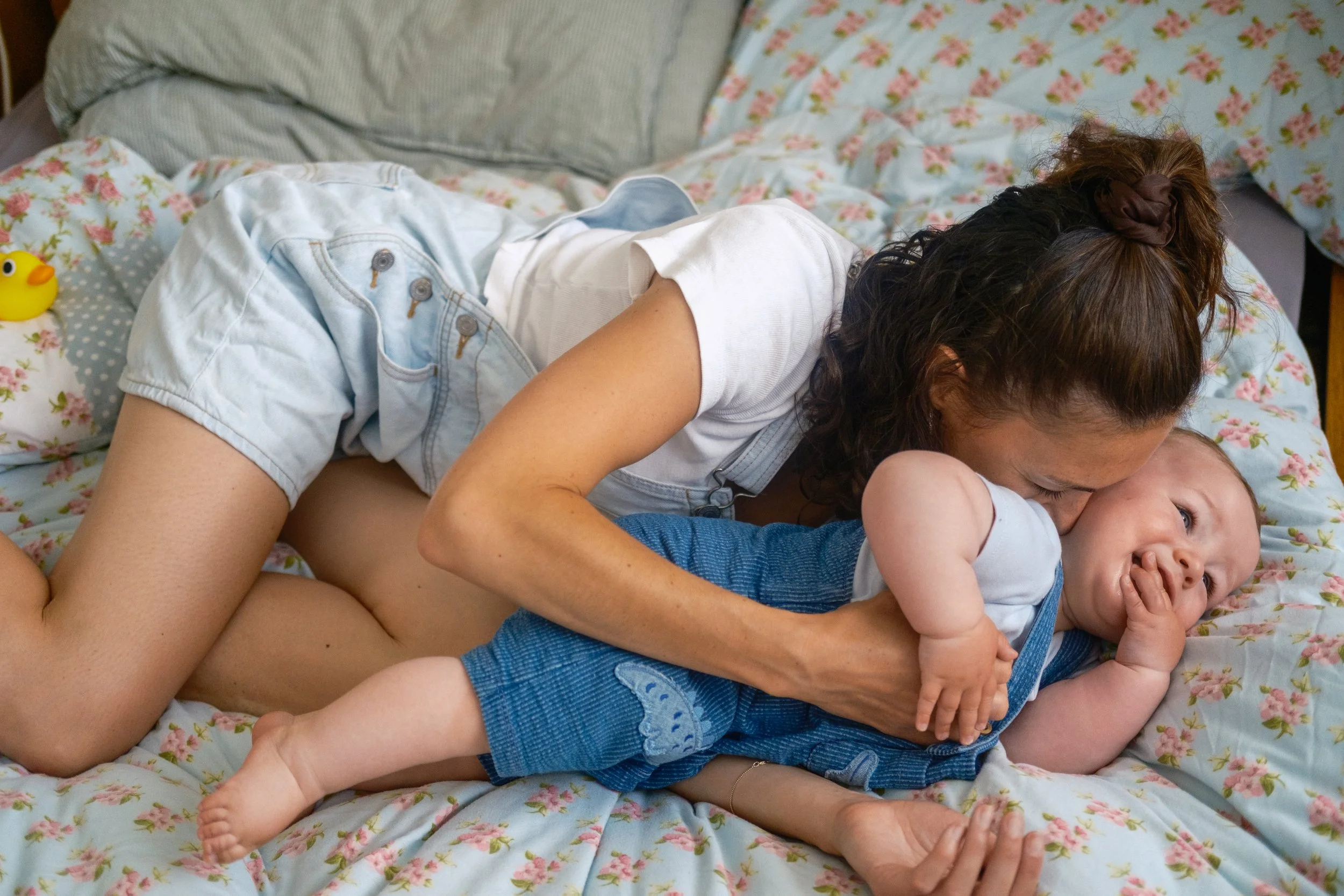 A woman and a baby lying on a floral bed, playing and cuddling.
