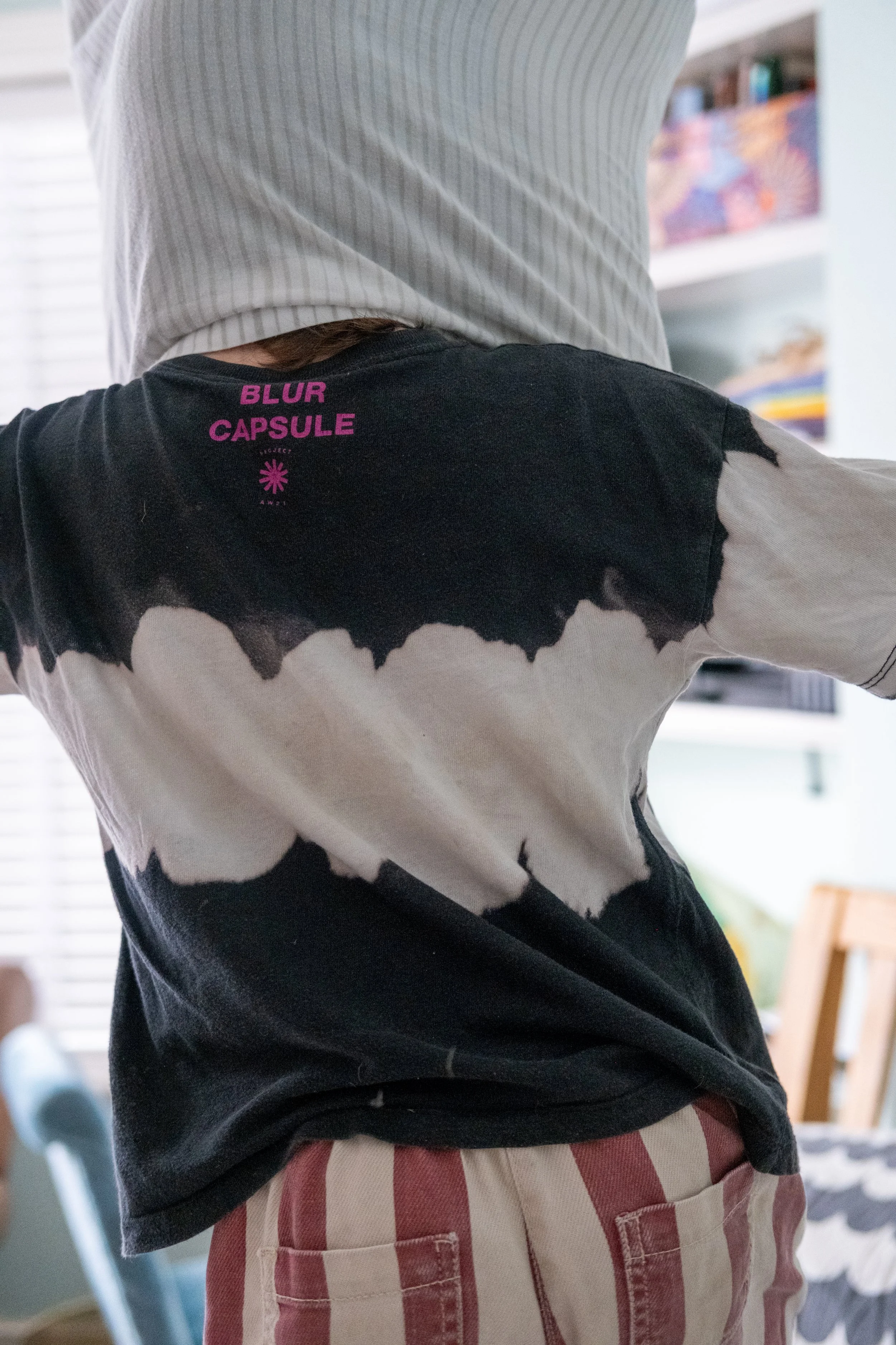 Person wearing a tie-dye t-shirt with purple text on the back and red-and-white striped shorts.