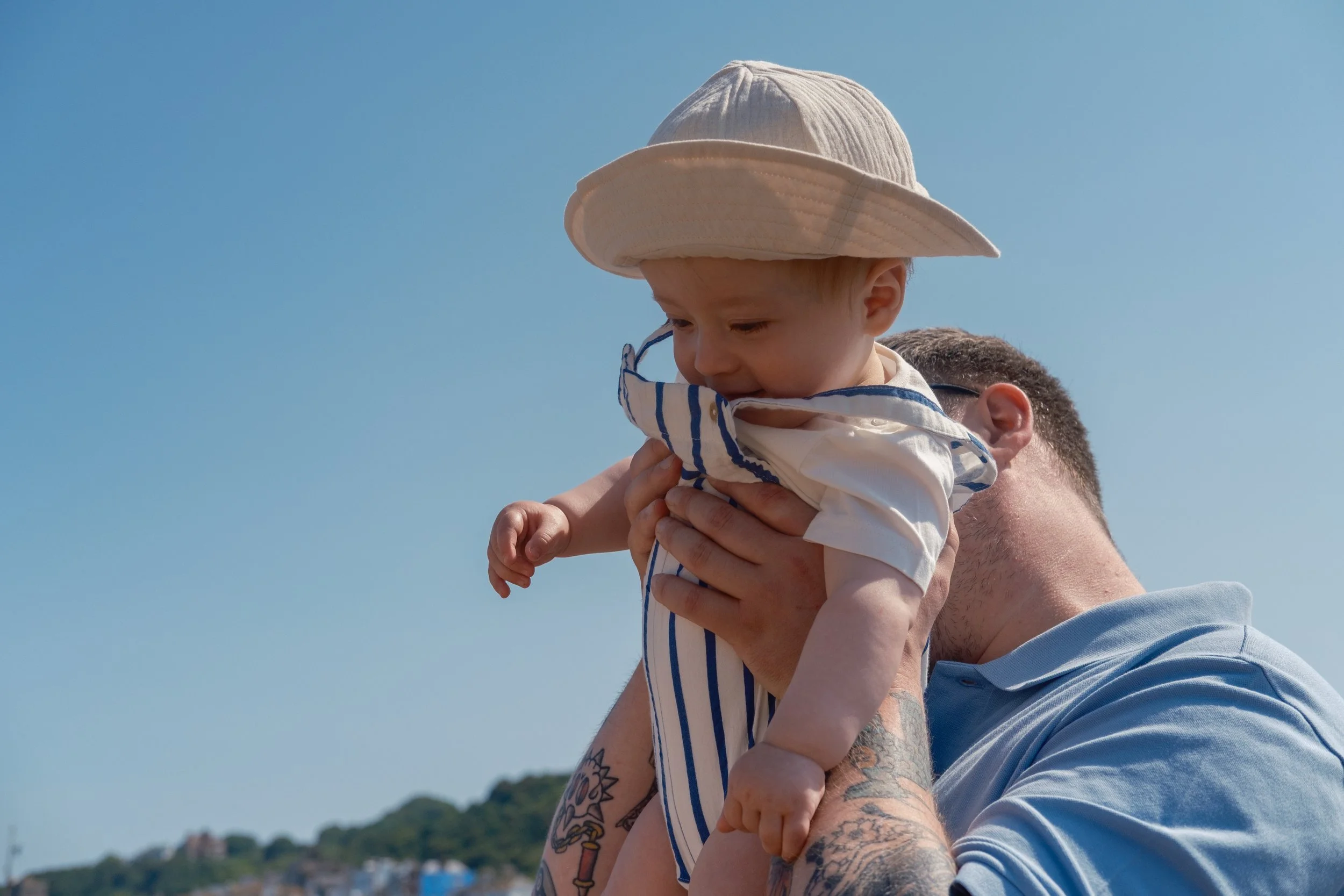 Man holding a young child outdoors under a clear blue sky.