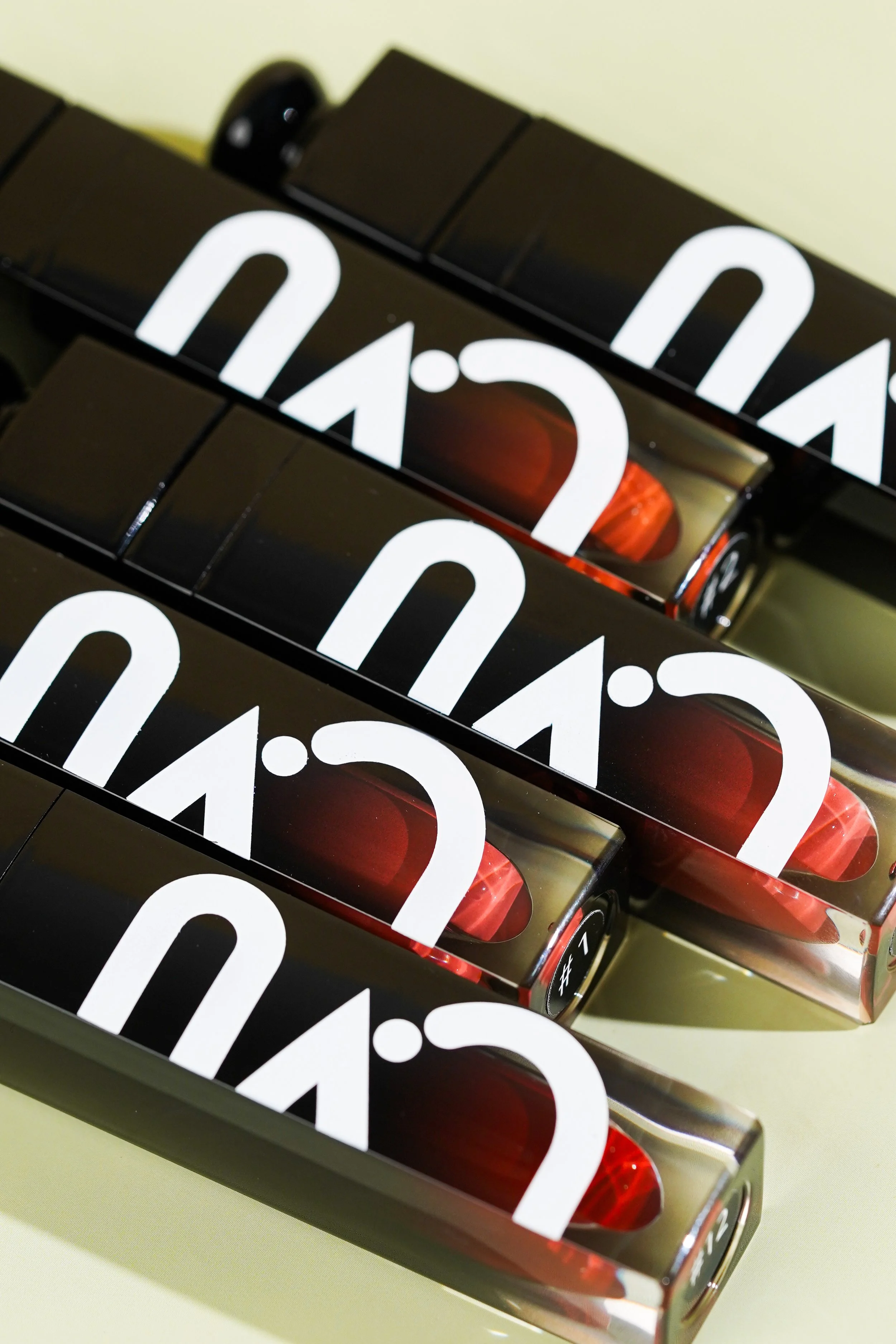 Close-up of multiple black and red lipstick tubes with white text, arranged diagonally on a light surface.