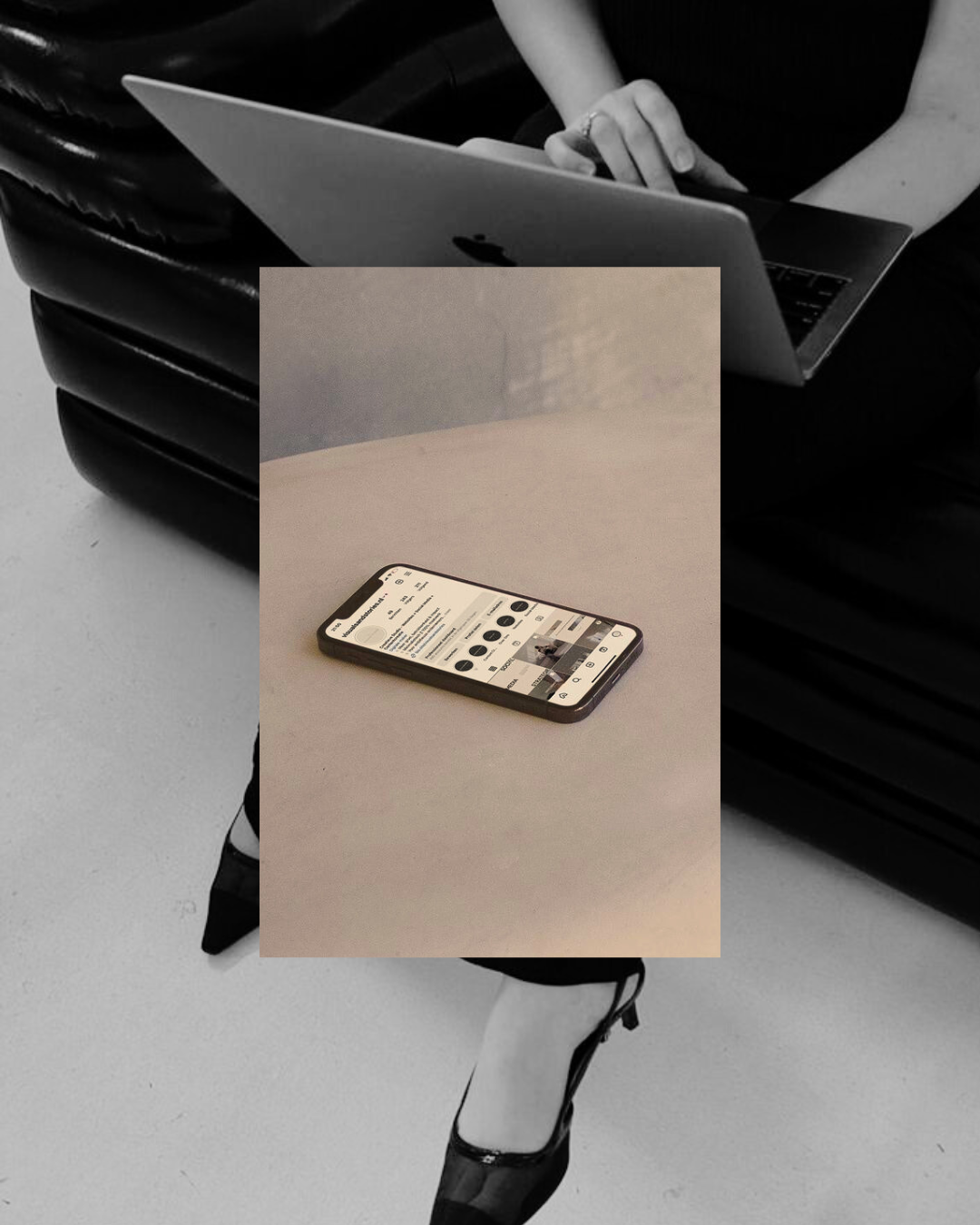 A woman sitting on a black leather couch working on a laptop, with a smartphone placed on a white table in front of her.