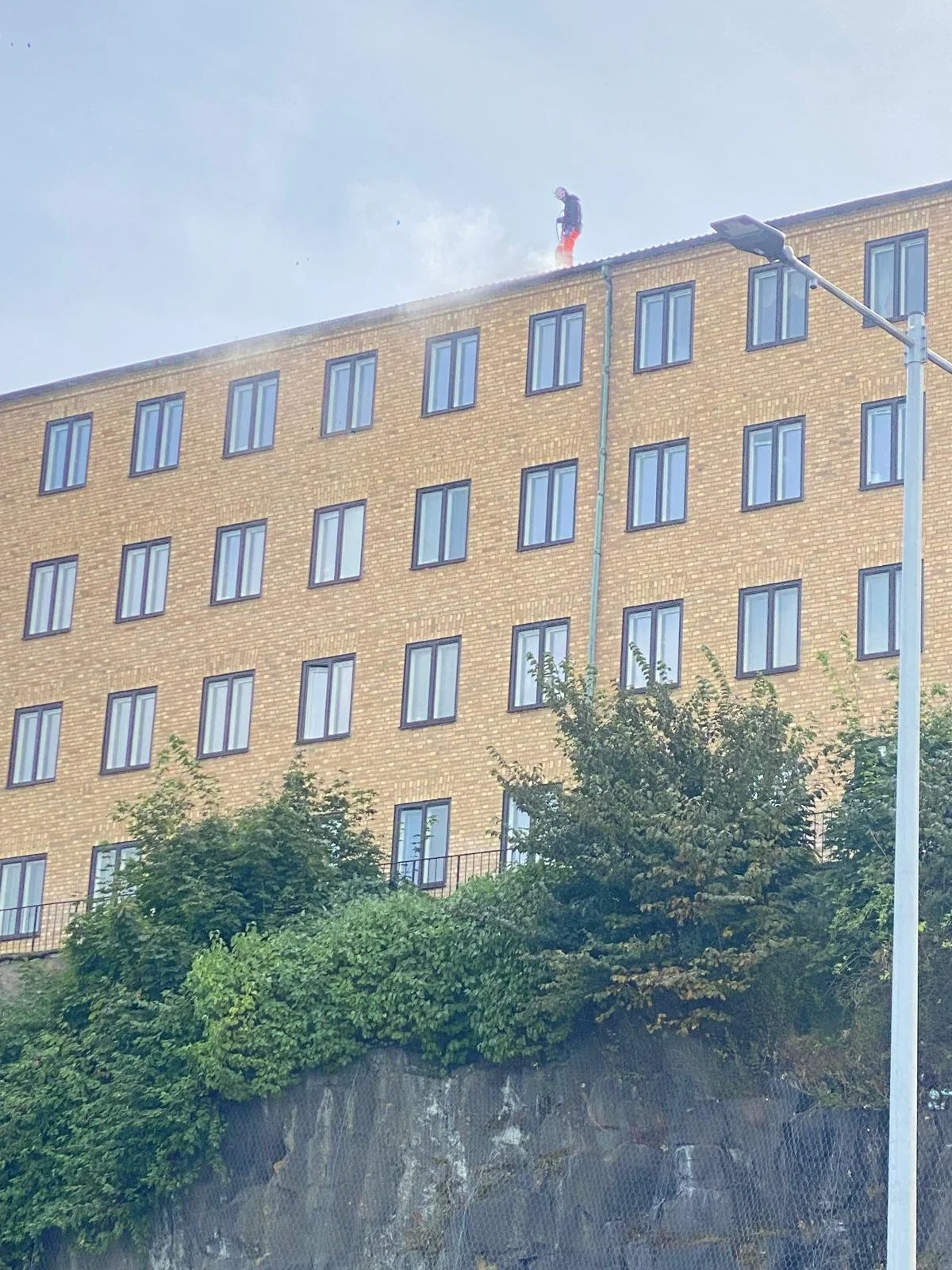 En person står på taket av en bygning som blir vasket med høytrykksspyler.