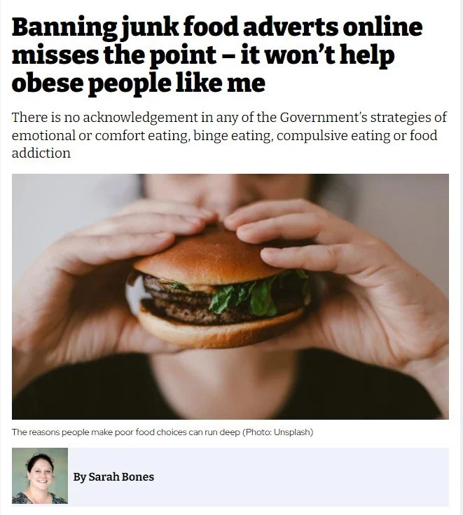 Article headline discussing how banning junk food ads online doesn't help obese people, with a close-up of a person holding a hamburger sandwich.