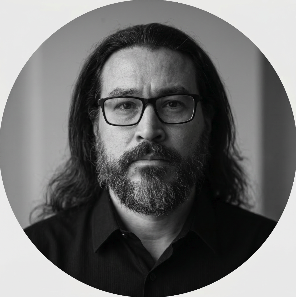 Black and white portrait of a man with long hair, a beard, mustache, glasses, and wearing a collared shirt.