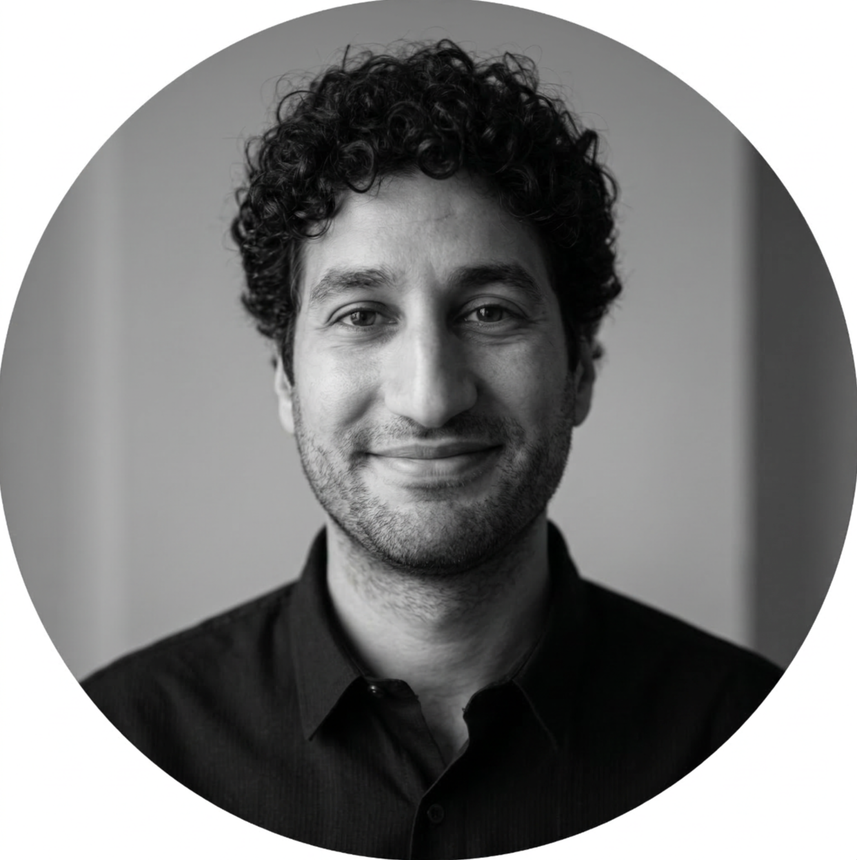 Black and white portrait of a man with curly hair, slight beard, smiling, wearing a dark collared shirt.