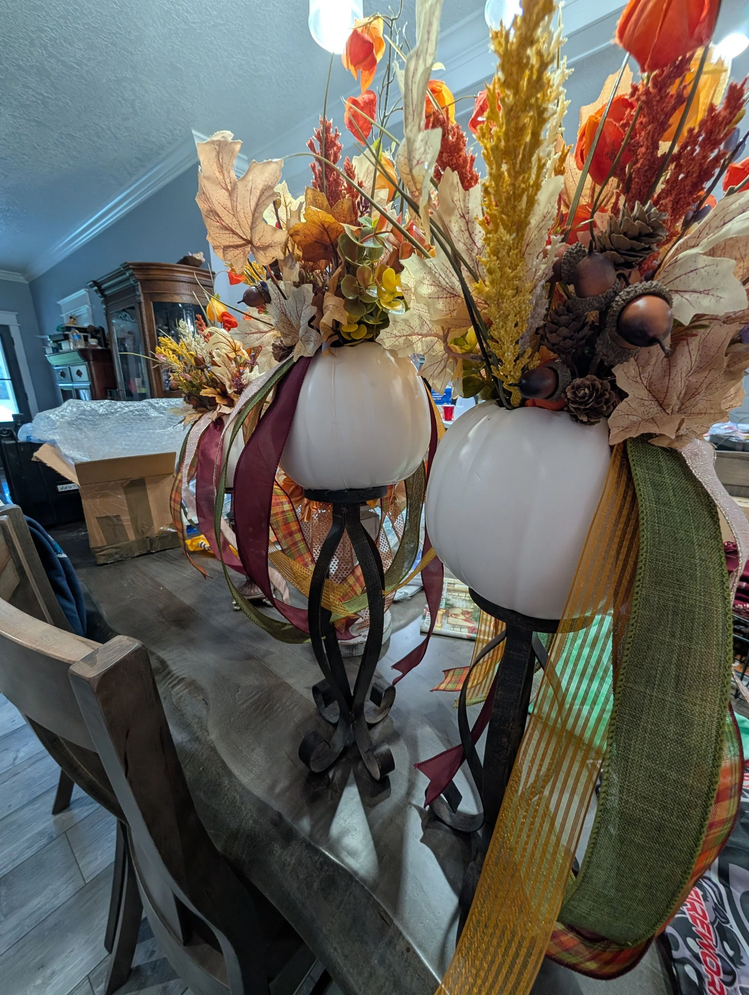 White pumpkin arrangements on black stands with long burgundy, olive, plaid and gold-toned ribbons.