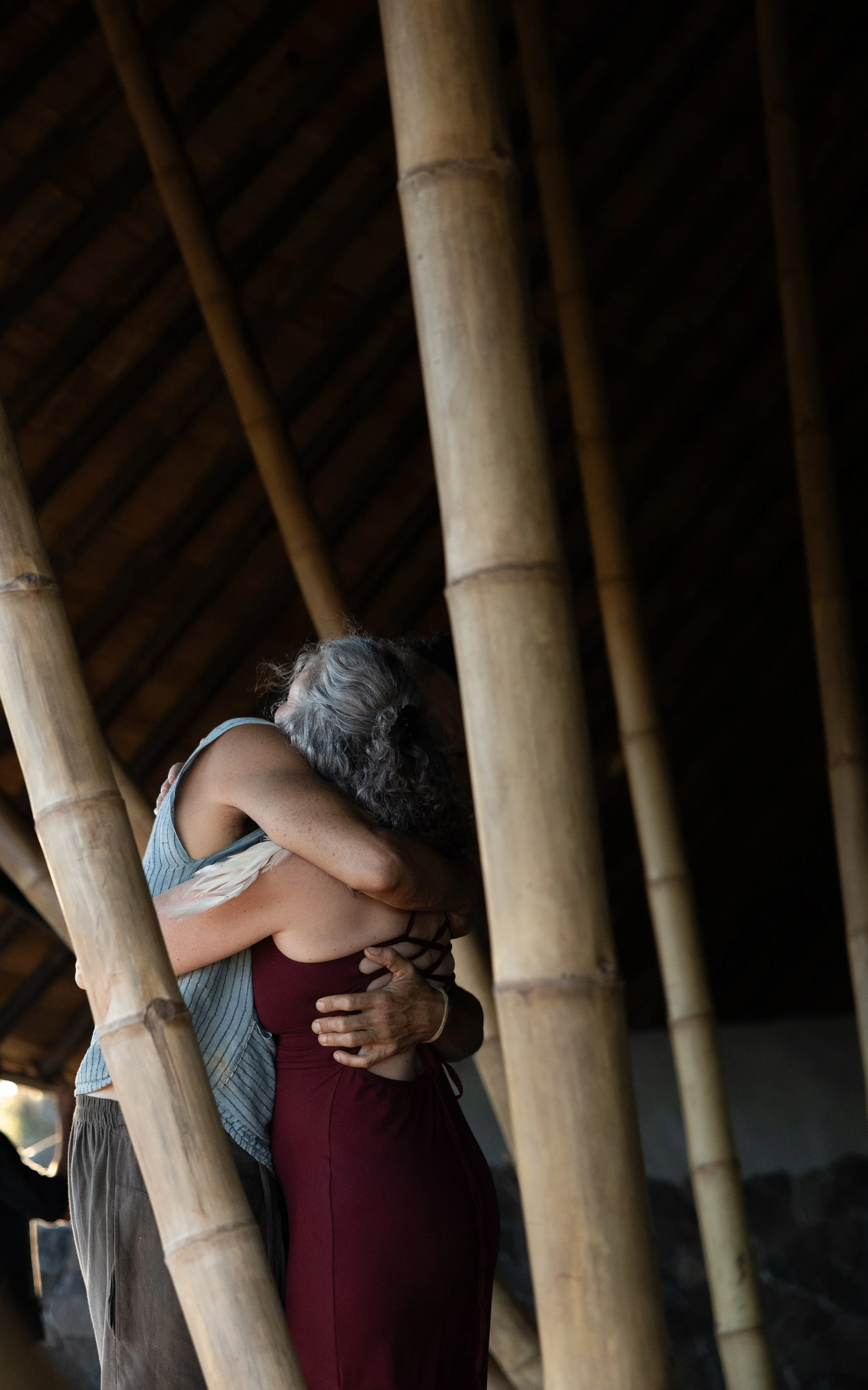 A man and a woman sharing a hug inside a bamboo structure with a thatched roof.