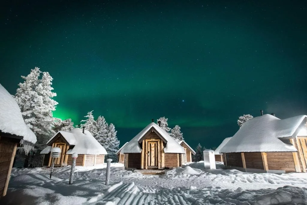 Snow-covered cabins in a winter landscape under the northern lights