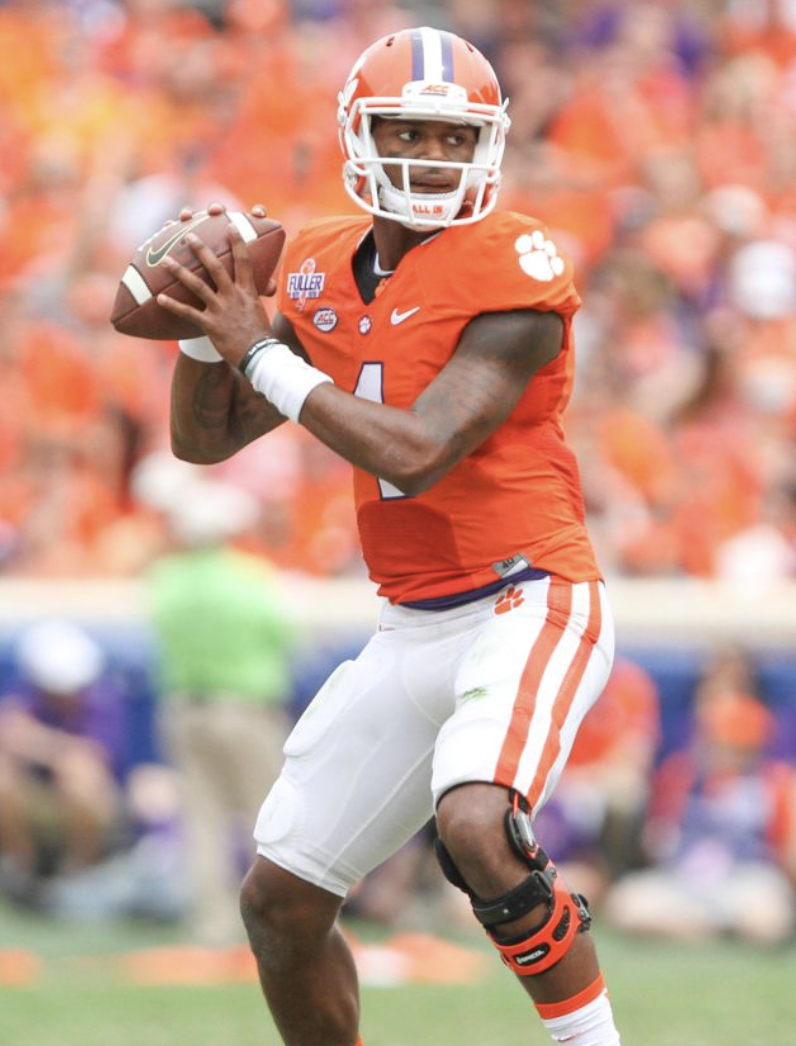 A football player wearing an orange jersey with the number 4, holding a football, on a field during a game.