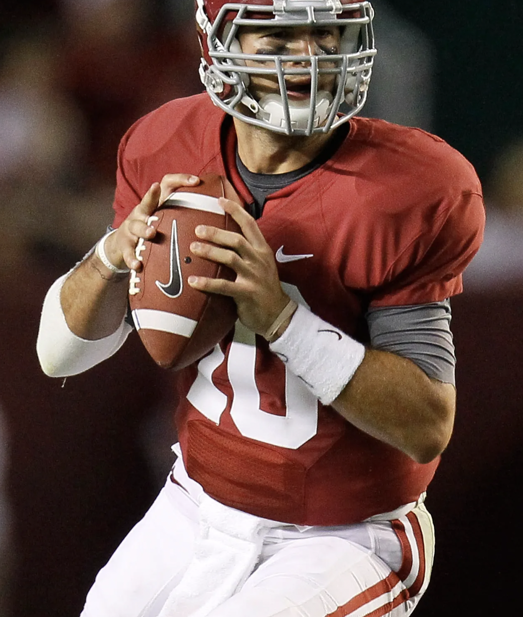 A football player in a red uniform with a gray helmet holding a football, ready to run on the field.