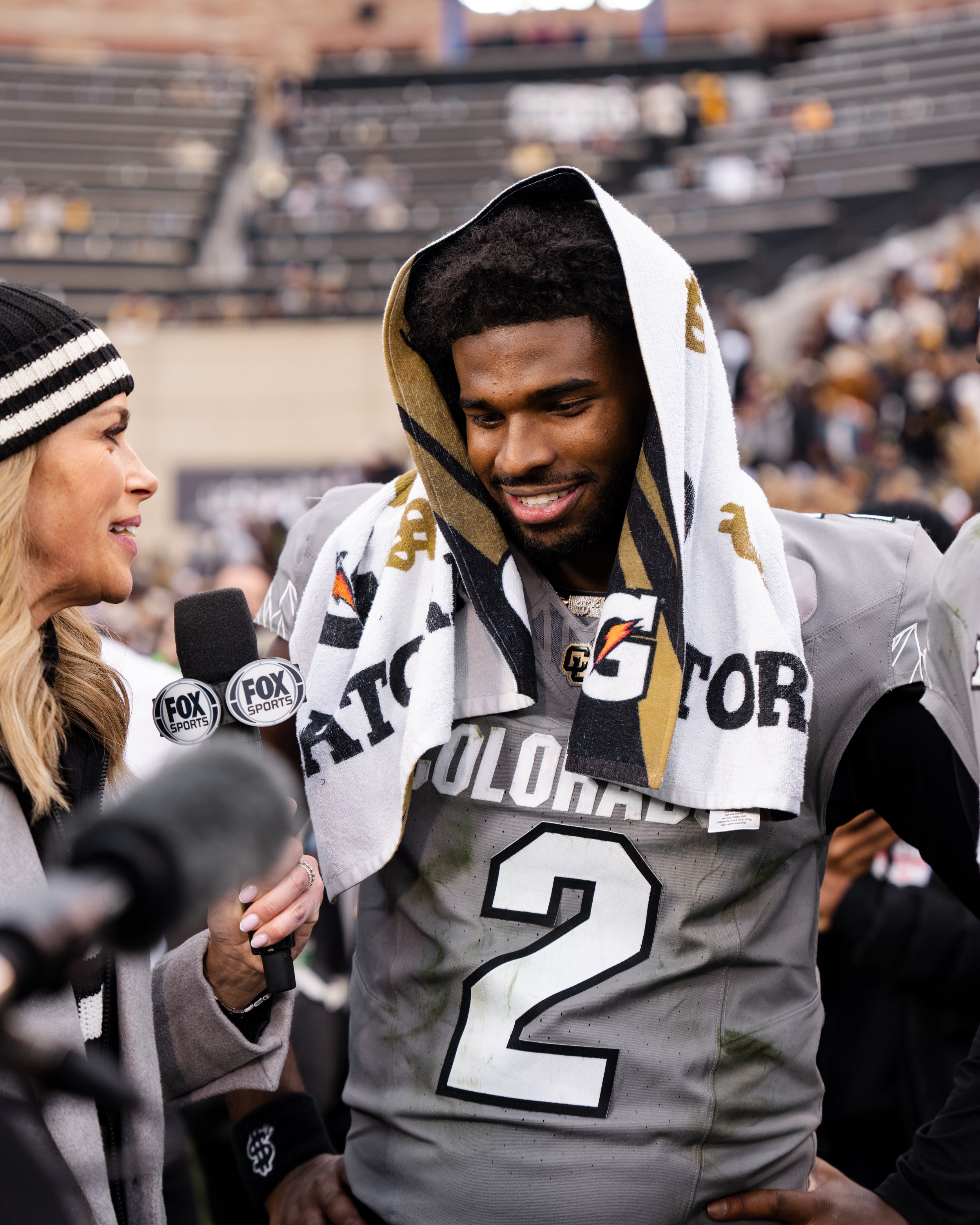 Football player wearing Colorado team jersey with number 2, being interviewed by a female reporter after a game, with a towel draped over his head.