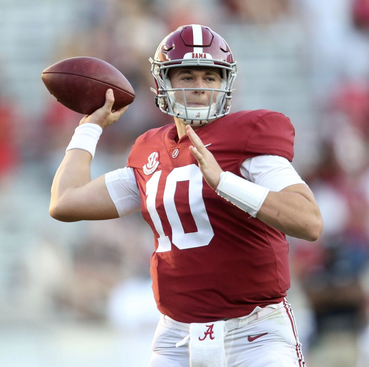 A football player in a red and white uniform with the number 10 is preparing to throw a football during a game.