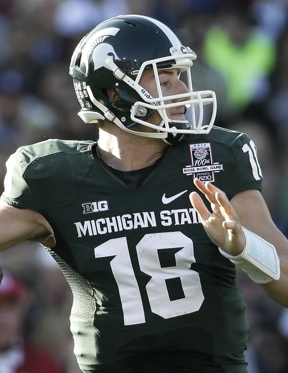 A football player in a green Michigan State uniform with the number 18, wearing a helmet with a Spartan logo, is preparing to throw a pass during a game.