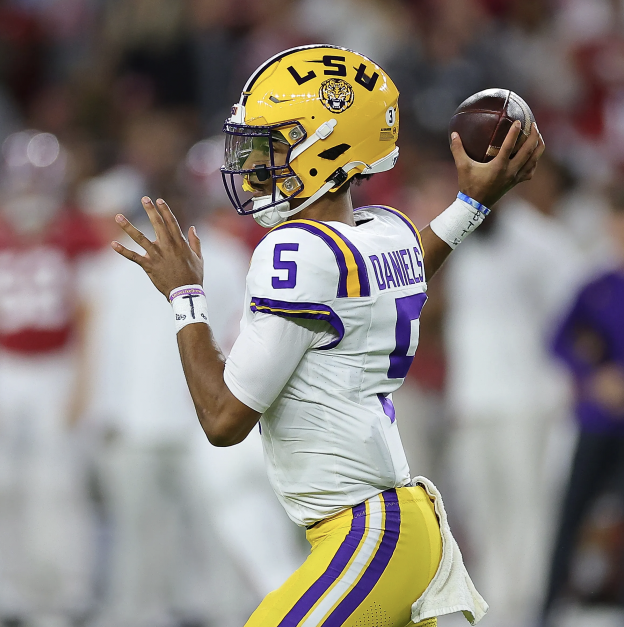 A football player wearing a yellow helmet with LSU logo, white jersey with purple and yellow accents, and yellow pants with purple stripes, preparing to throw a football during a game.