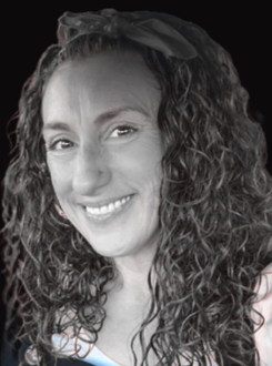 Black and white photo of a woman artist with curly hair, smiling, wearing a headband.